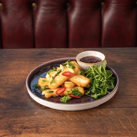 A plate of Halloumi fries with a small bowl of dipping sauce on a table.