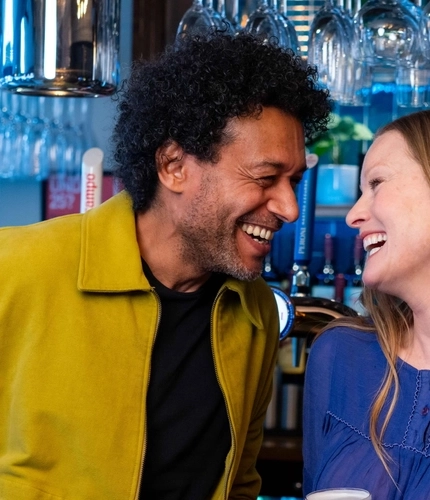 A couple of people next to a bar enjoying drinks.