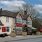 The exterior facade, signage, and seating area of The Hussey Arms in Brownhills, with picnic tables, planter boxes, and string lights.