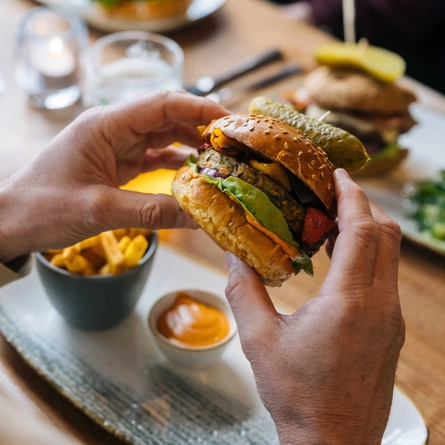 A close up image showing a person sat at a table within the interior restaurant seating area holding a burger at a Heritage venue.