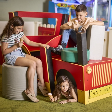 Three children playing on a wooden tractor in the play area at a Farmhouse Inns venue, and holding ice cream served in waffle cones.