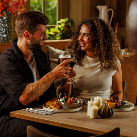 An image of 2 people enjoying 2 Game Night Main dishes and drinks within the interior restaurant and seating area at The Foundry Bell.