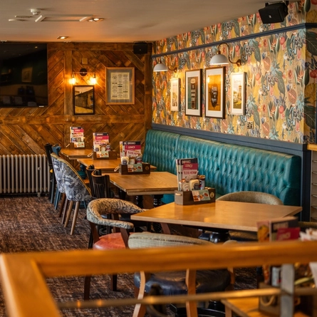 The interior restaurant seating area of The Merlin, with upholstered booth seating, wooden tables, TV and framed artwork on the walls, and a radiator.