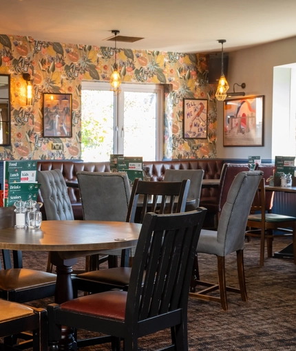 The interior restaurant seating area at the Rudds Arms in Marton-In-Cleveland; with an upholstered booth seat in the corner by the windows, and framed artwork on the walls.