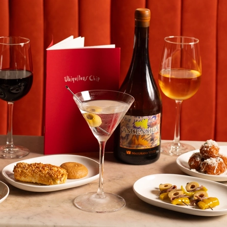 An advertising image of a selection of snack dishes and various drinks sat on a table within the interior restaurant and seating area at The Ubiquitous Chip.