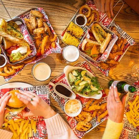 An overhead image showing several mains and sharer dishes sat on a table with a selection of drinks at a Flaming Grill venue.