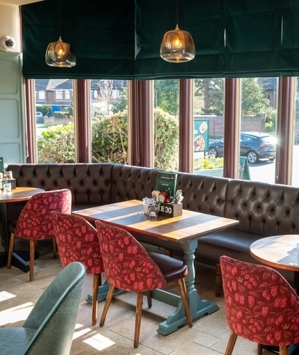 An interior restaurant seating area at the Golden Hind, with a long, upholstered booth seat running along the large bay window.