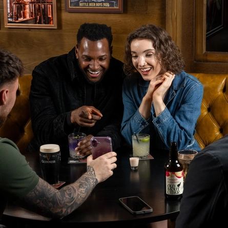 A group of people seated around an indoor table with a selection of drinks and shots in front of them.