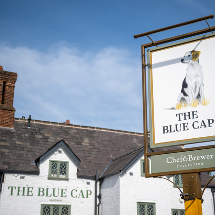 A close up view of the exterior pub sign of The Blue Cap, featuring an illustration of a black and white dog above the words "The Blue Cap".