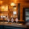 A close up view of the wood panelled bar inside The Kings Arms in Sandford-On-Thames, with spherical lights hanging above the counter, and bottles of alcoholic spirits on wooden shelves behind the bar.