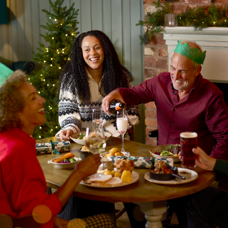 An image of 4 people sat around a table within the exterior restaurant and seating area enjoying various main dishes and drinks being poured available at Chef & Brewer venues.