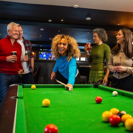 An image of a group of people enjoying drinks and a game of pool within a Flaming Grill venue.