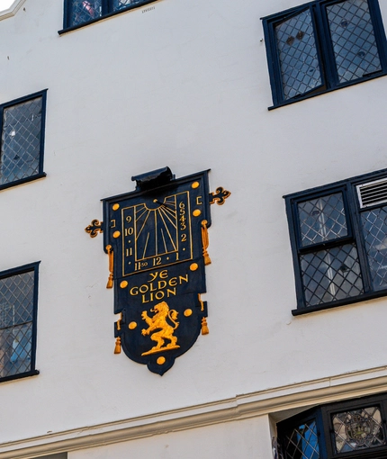 A view looking upwards at the exterior facade of The Golden Lion, with a large black and gold clock on the wall between the upper windows.