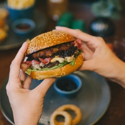 A pair of hands holding a burger over a plate.
