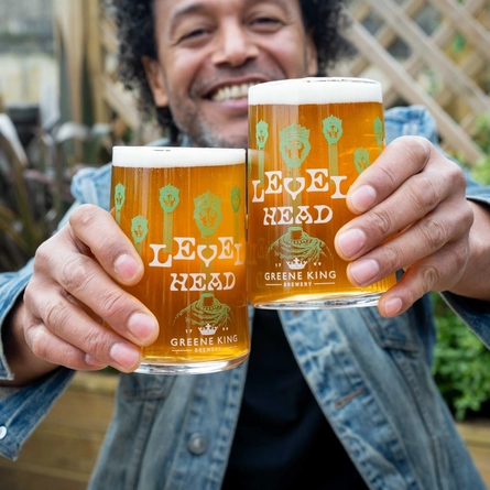 A man holding two pints of Level Head at a table in a beer garden.