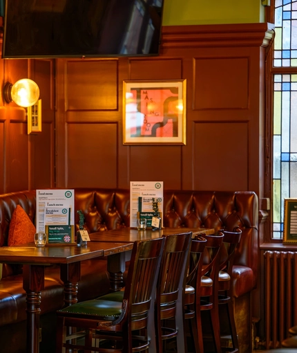 A close up view of restaurant tables and an upholstered corner seat inside The Globe; with framed artwork and a TV on the wood panelled walls above.