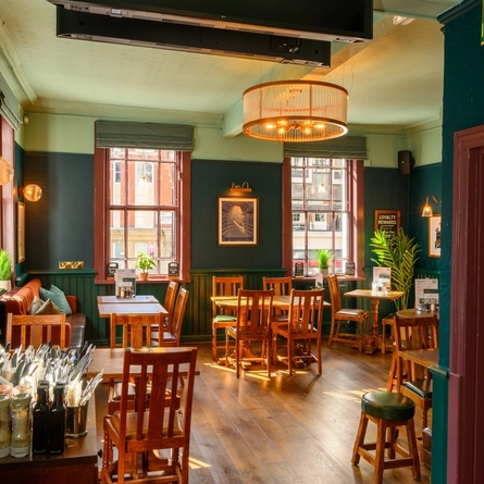 An interior restaurant seating area at the Coach & Horses; with wood panelled walls, large windows, and an upholstered booth seat in the corner.