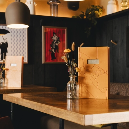 An image focusing on the menu and dried floral arrangement sat on one of the tables within the interior restaurant seating area at The Foundry Bell.
