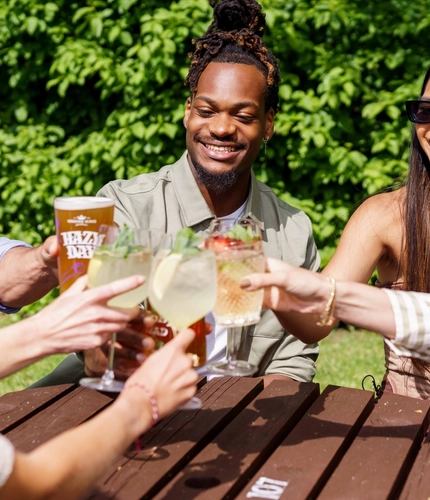 A mixed group of people, sitting at an outdoor table, enjoying a variety of drinks and conversation.