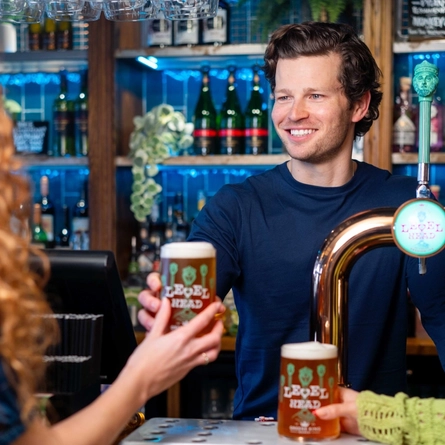 A man behind a bar serving a pint of Level Head.