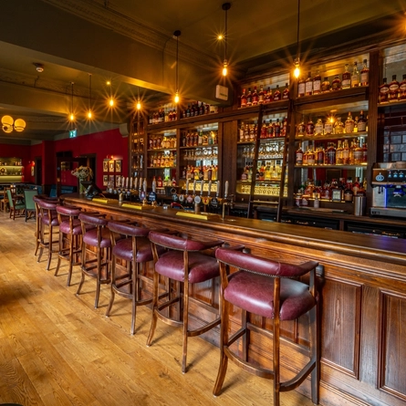 The wood panelled bar and interior restaurant seating area at The Beehive Inn, with upholstered chairs and bar stools, and a TV on the wall.