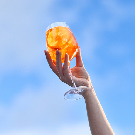 An image of a glass of Aperol Spritz being held up in the air against a blue sky background at a Chef & Brewer venue.