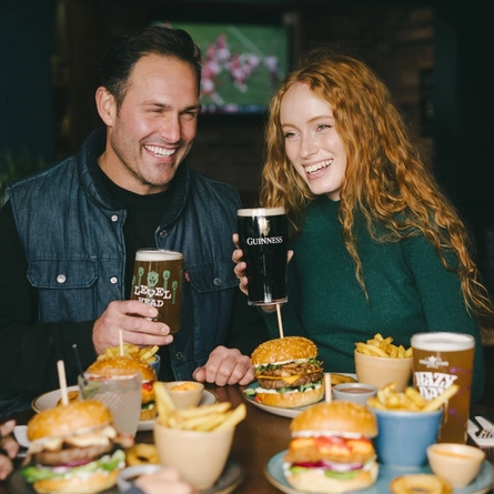 A lifestyle image of 4 friends sat within the interior restaurant seating area enjoying Burger dishes and various drinks available at Urban Core venues.