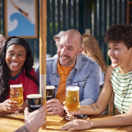 A mixed group of people seated at an outdoor table holding drinks.