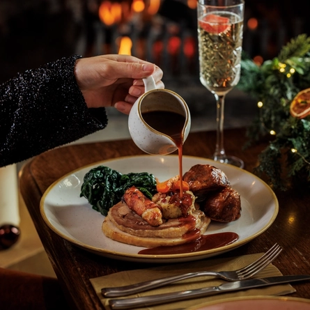 An image of gravy being poured onto a plated Festive roast turkey dish and a glass of sparkling white wine sat on a table