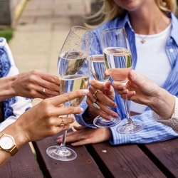 A close up image of glasses of Prosecco being held during a Fizz Friday Offer within an exterior beer garden seating area.