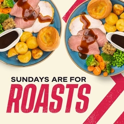 Promotional banner featuring the text “Sundays Are for Roasts” alongside two traditional roast dinners on a light beige background with bold red chevron graphics. The plates include slices of roast beef and turkey topped with gravy, served with roast potatoes, Yorkshire puddings, peas, carrots, broccoli, stuffing, and a jug of extra gravy.
