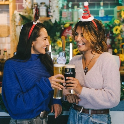 An image of 2 friends enjoying drinks stood at the interior bar within a Greene King venue.