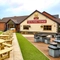 The exterior facade, signage and beer garden seating area of The Flying Horse in Heald Green, featuring wooden picnic tables and a children's play area.