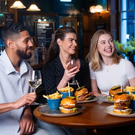 A group of friends sat in the interior restaurant and seating area in a Urban Social venue, enjoying burger main meals and drinks.