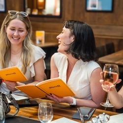 A group of people enjoying drinks and viewing the menu within the interior restaurant seating area during The Durell Arms launch party.