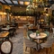 Some tables in The Rockingham Arms restaurant area, with foliage hanging from the windows and lights and the bar in the background.