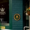 A close up view of the Greene King logo on a glass door of the Malvern Tavern, and on a circular green and yellow plaque on the brick wall next to it.