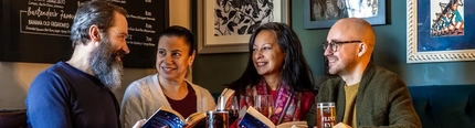 A group of people sitting at a table full of books with drinks.