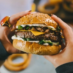 A close up product image showing a burger being held by a customer within the interior restaurant seating area at an Urban Core venue.