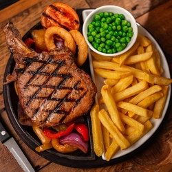 A image of a served Toma Pork steak main with chips, peas, onion rings and a grilled tomato served at Flaming Grill venues. 