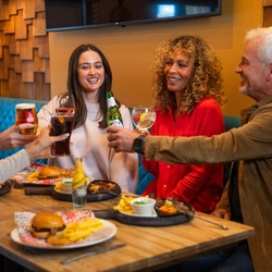 A mixed group seated at an indoor table holding drinks.  There are plates of food in front of them.