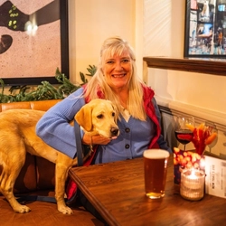 An image of a customer with drinks sat with a dog at a table within the interior seating area of The Crabtree.