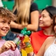 Two children sitting next to each other with a bottle of Fruitshoot in a "Cheers" pose.
