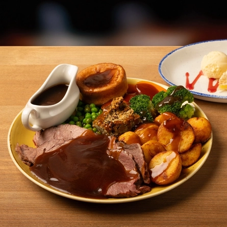 A plated roast dinner and dessert on a wooden table.