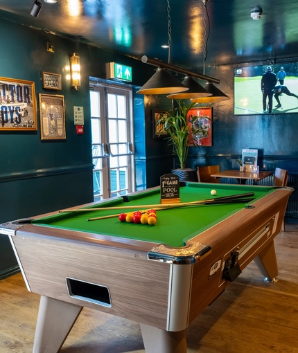 The interior restaurant seating area of the Cock & Pye, with a pool table, and a TV on the wall.