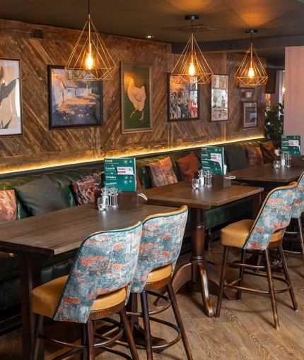 An interior restaurant seating area at the Rudds Arms; with a long, upholstered booth seat against one wall, with framed artwork above it.