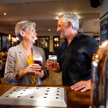 An image of 2 people stood at the interior bar with 2 drinks at a Community Pubs With Food venue.