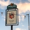 A close up view of the exterior pub sign of the Malvern Tavern, featuring an illustration of a red coat of arms with four crescent moons, filigree patterns and a dogs head, above the words "Malvern Tavern, Shirley".