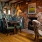 An interior restaurant seating area at The Kings Arms in Sandford-On-Thames, with wooden flooring and beams, upholstered chairs, and a brick fireplace with a log burner.