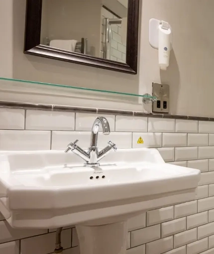 The interior hotel bathroom with a sink, mirror and shower at the Cedars Inn.